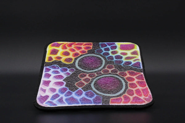 Close-up of Moodmats X Kaj Beck smoke accessories with intricate patterns and vibrant colors on textured fabric.